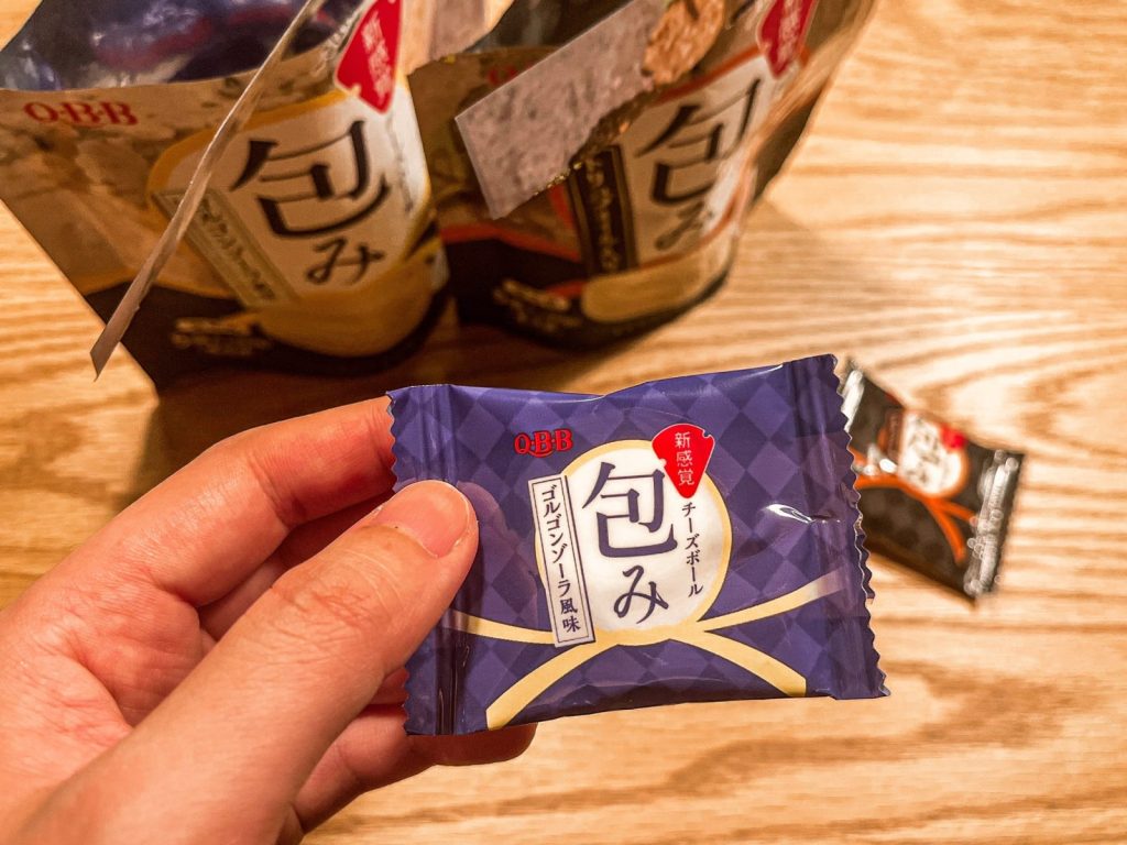 「QBB チーズボール包み」のゴルゴンゾーラ風味の個包装を手に持っている。