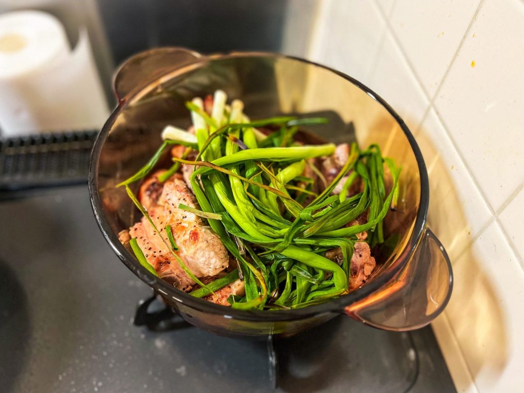 焼いたスペアリブを鍋に移して調味料と煮込んでいる。焦がしたネギが上に乗っている。