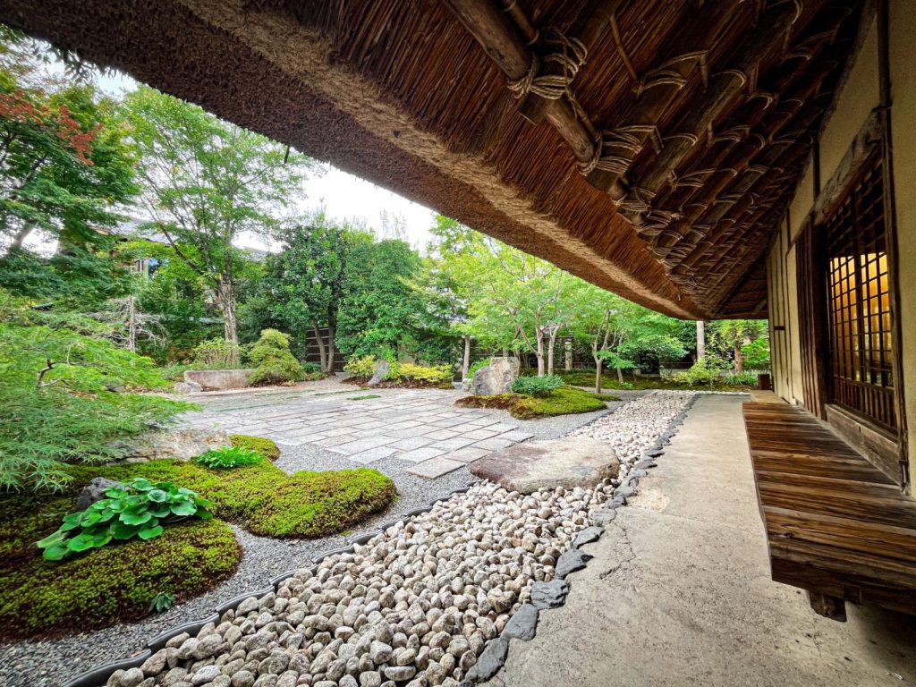 パンとエスプレッソと嵐山庭園の中にある日本庭園。右側の茅葺の建物には縁側があり、そこで座りながら石畳や木々の庭園が眺められる。
