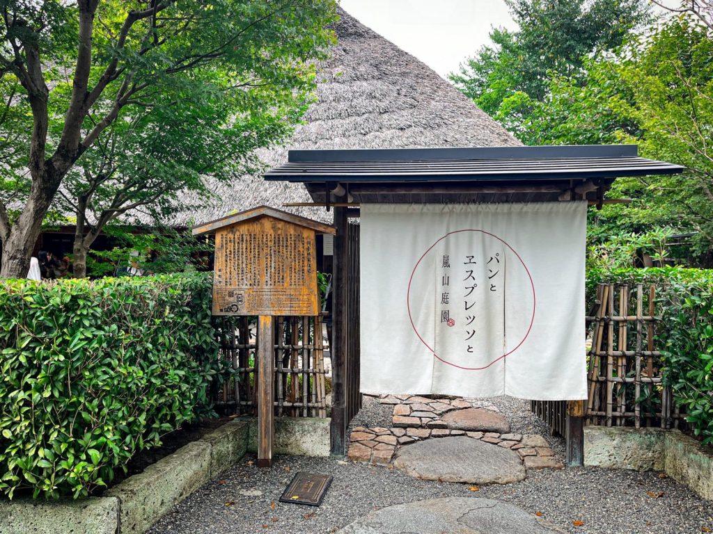 パンとエスプレッソと嵐山庭園の入り口。茅葺の建物は垣根で覆われており、その入り口にはのれんが掛かっている。