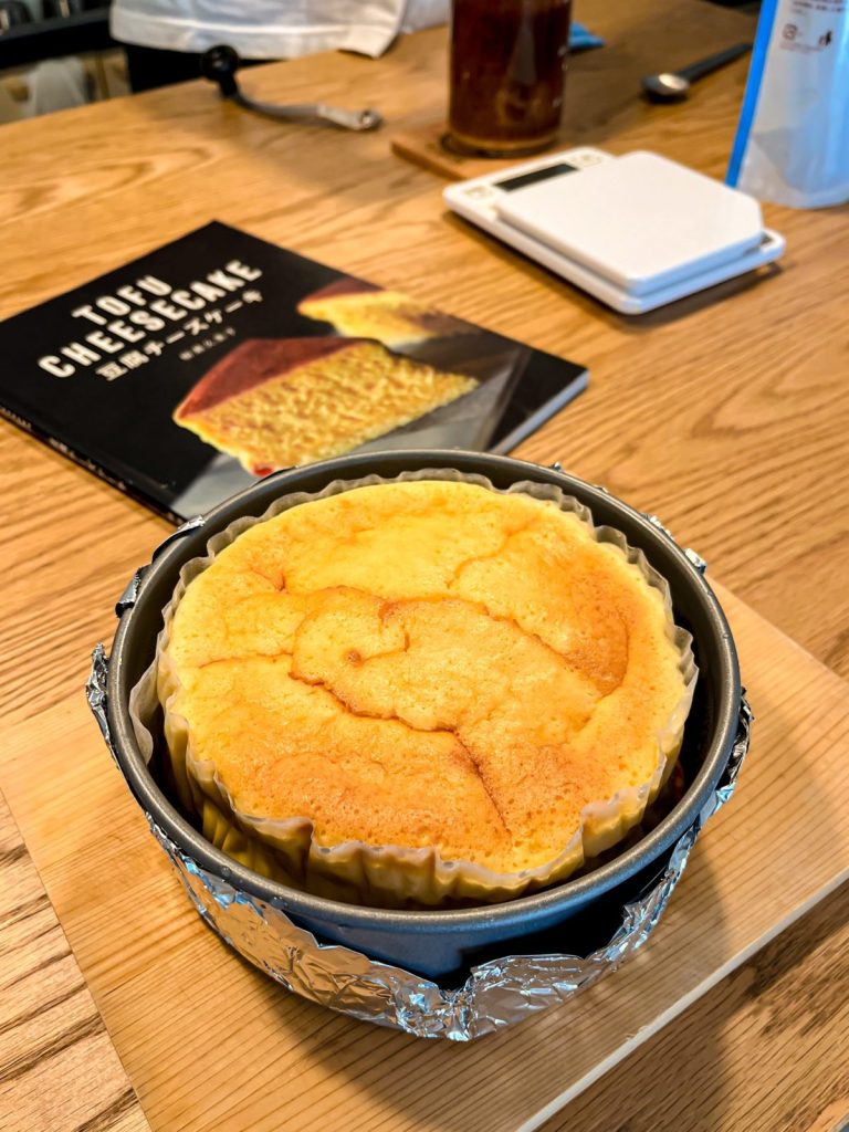テーブルの手前に焼きたての豆腐のスフレチーズケーキがある。その奥に「豆腐チーズケーキ」のレシピ本が置いてある。