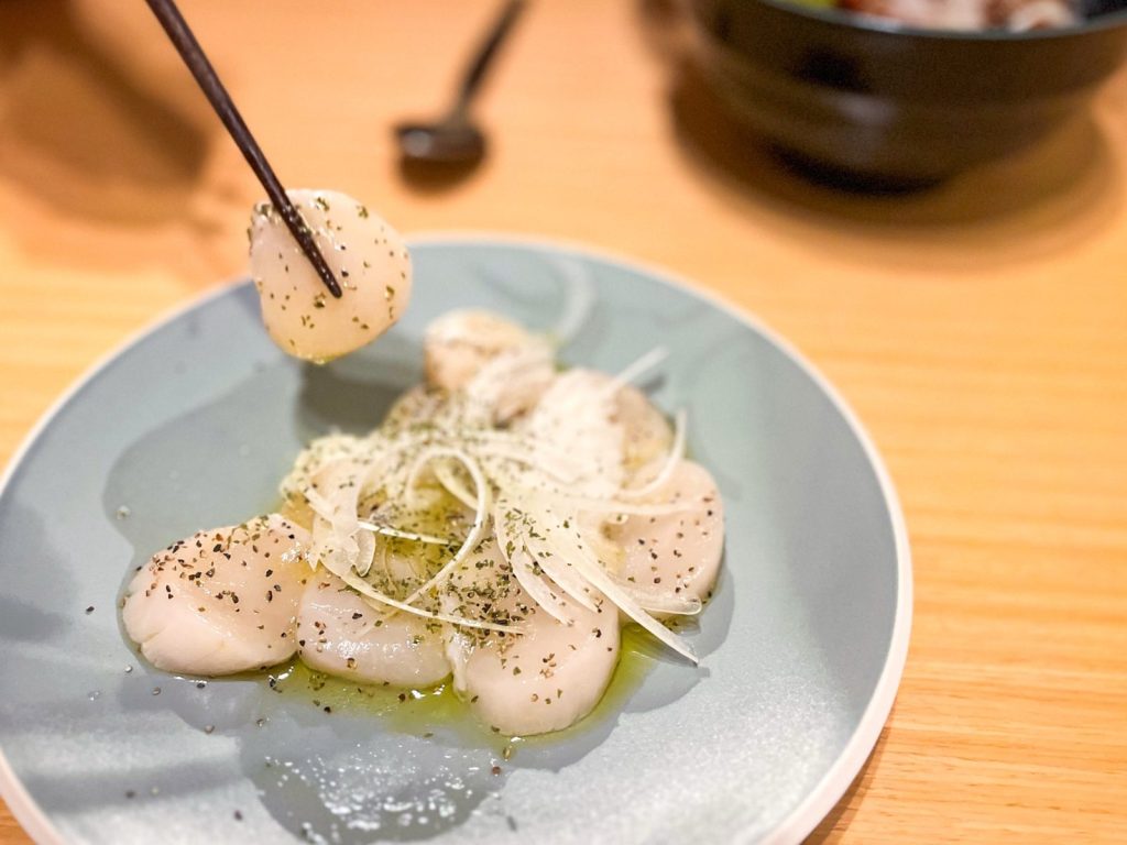 ホタテのカルパッチョを箸でつまんでいる。