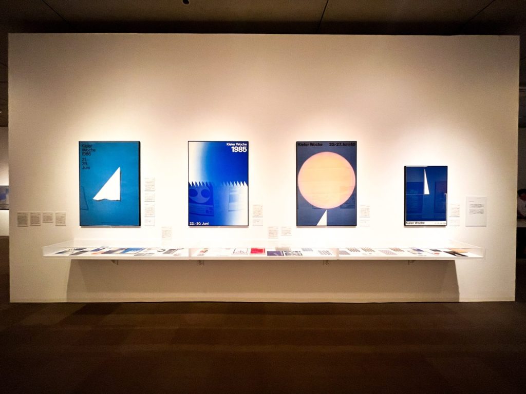 展覧会の様子。壁にはポスターが展示されている。テーブル式のスペースには小さめのグラフィックが並んでいる。